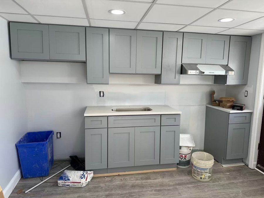 Grey shaker cabinets and counter fitted in a drop ceiling room, compound bucket still on the floor